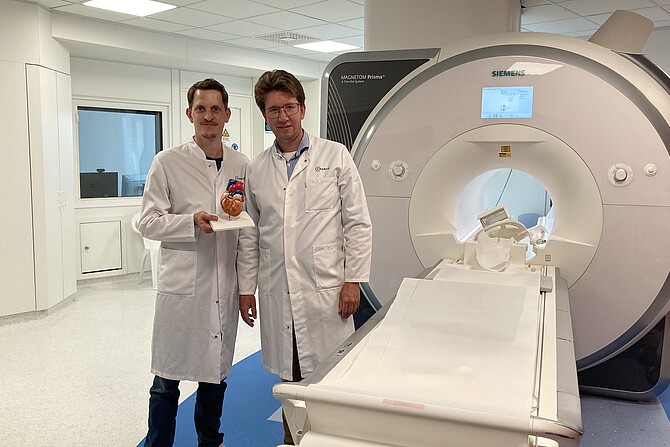 PD Dr. Simon Hellwig und Prof. Dr. Jan F. Scheitz neben einem MRT-Gerät, Prof. Scheitz hält ein Modell des Herzens