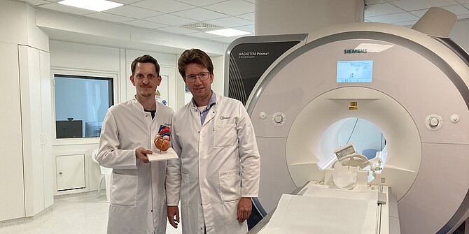 PD Dr. Simon Hellwig und Prof. Dr. Jan F. Scheitz neben einem MRT-Gerät, Prof. Scheitz hält ein Modell des Herzens