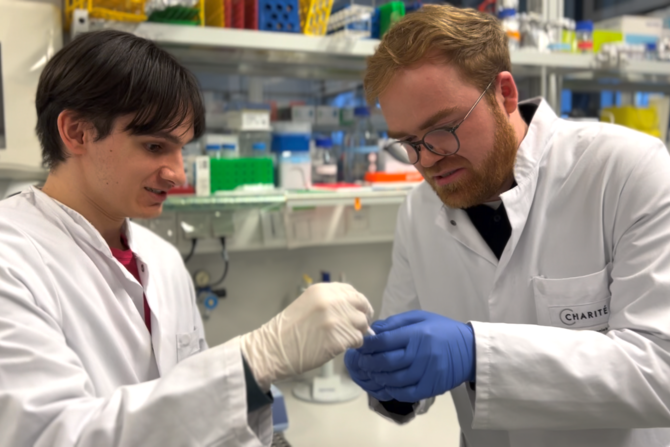 Zwei Forscher stehen nebeneinander in einem Labor und arbeiten gemeinsam ein einem mRNA Forschungsprojekt
