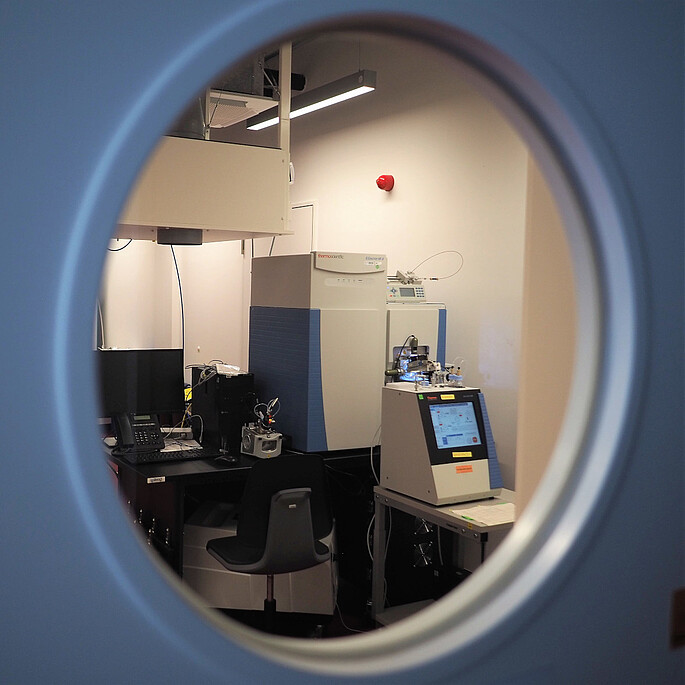 Blick in durch ein Labortürfenster auf ein LC-Massenspektrometer Setup